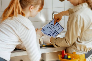 İki kişi dijital tablet üzerinde bir oda düzenini gözden geçirip, bir ev yenileme projesi planlıyor. Oda bir çamaşır odası ve lavabo içeriyor..