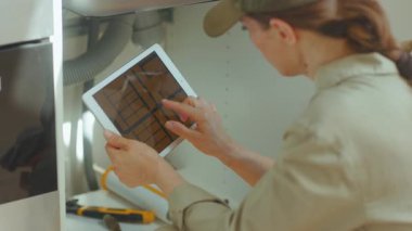 Tesisatçının elinde tablet tasarımı, lavabonun altındaki tesisat teftişi modern bir mutfakta doğru iş ve sorun çözme garantisi var..