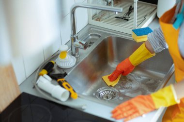 Eldivenli eller paslanmaz lavaboyu, yakınlardaki su tesisatını tarar inatçı bir mutfak giderini temizleme ve açma çabalarını gösterir..