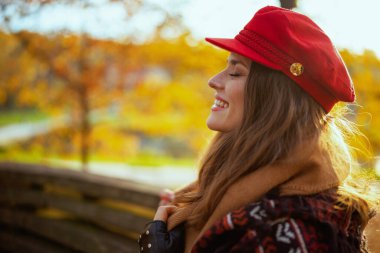 Merhaba sonbahar. Şehir parkında bankta oturan kırmızı şapkalı 40 yaşında mutlu bir kadın..