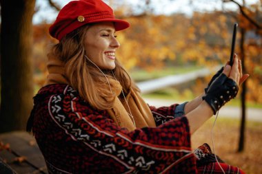 Merhaba sonbahar. Kırk yaşında kırmızı şapkalı, atkı ve eldivenli, akıllı telefon kullanan ve şehir parkında bankta otururken video konferansı yapan son moda bir kadın..