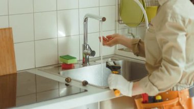 Tesisatçı, onarımdan sonra paslanmaz çelik lavabodaki krom musluğu kontrol eder. Su serbestçe akıyor, bu da düzeltmeyi doğruluyor. Civardaki anahtarlar ve aletler tesisatta uzman olduğunu gösteriyor..