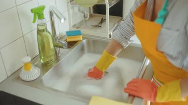 Sabunlu suyla dolu bir lavabo tıkanıklık olduğunu gösteriyor. Kadın önlüğü, kanalizasyonu temizlemeyi umuyor. Temizlik spreyi, sünger ve fırça yardımı. Genel tesisat sorunu.