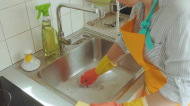 Kadın, sabunlu bir mutfak lavabosunu temizliyor. Potansiyel bir su tesisatı sorununu hallediyor. Sünger ve temizlik çözeltisi eylem için hazır.