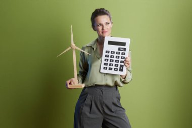Bir kadın elinde bir hesap makinesi ve rüzgar türbini, sürdürülebilir finansman, yeşil enerji yatırımı ve geleceğe yönelik düşünce taşımaktadır..