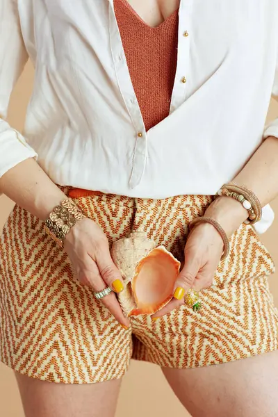 Plaj tatili Beyaz bluzlu kadına yakın çekim ve deniz kabuklu bej arkaplanlı şort..