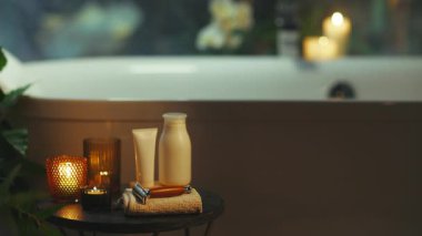 A serene, dimly lit bathroom showcases a freestanding bathtub, complemented by a small table featuring glowing candles, a white tube, bottle, and a safety razor, evoking a tranquil spa-like ambiance for personal care.