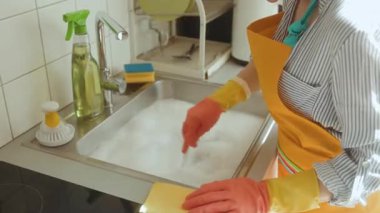 Sabunlu bir lavabo tıkanmış bir kanalizasyona işaret ediyor. Kadın suyu karıştırıyor, sıhhi tesisat sorunuyla karşı karşıya. Yakınlarda bir çözüm bulmak için bez ve sprey şişesi temizliyorum..