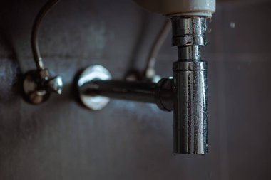 Lavabonun altında su damlacıkları olan sızdıran krom drenaj borusu bir tesisat sorununa ve bakım ihtiyacına işaret ediyor..