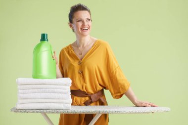 Yeşil deterjan şişesi tutan, gülümseyen, temiz havlu yığınının yanında duran mutlu kadın..