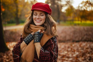 Merhaba sonbahar. Şehir parkında kırmızı şapkalı, eşarplı ve eldivenli rahat genç bir kadın..