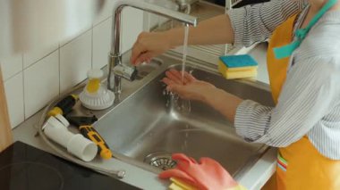 Bir kadın mutfak lavabosundaki su ısısını kontrol eder. Etrafı aletlerle çevrilidir. Tesisat onarımından sonra ev bakımı: DIY ev geliştirme.