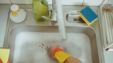 Yakın plan, sabunlu bir mutfak lavabosu ve tıkanmış bir lavabo olduğunu gösteriyor. Lastik eldivenler tesisat sorununu halletmek için hazır. Yakınlarda temizlik malzemeleri var..