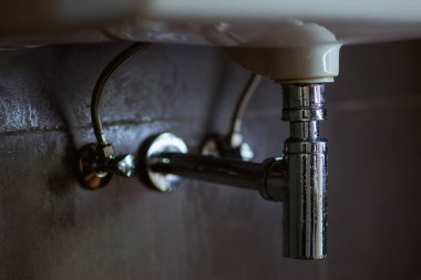 Beyaz banyo lavabosunun altındaki krom tesisat esnek ikmal hatları ve P-trap içeriyor. Bakım ya da potansiyel tesisat onarımı öneriliyor..