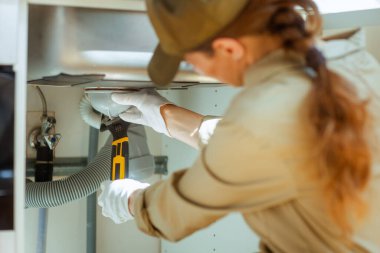 Tulum giymiş bir tesisatçıya yakın çekim. Ev onarımı sırasında lavabonun altına sarı ve siyah bir anahtarla beyaz boruyu sıkıyor..