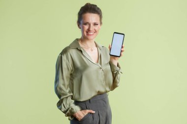 Gülümseyen bir kadın elinde beyaz ekranlı bir akıllı telefon tutuyor, açık yeşil arka planda bir iş ya da promosyon içeriği öneriyor..