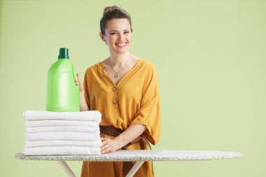 Sarı elbiseli mutlu kadın havluların yanında yeşil bir şişe deterjan tutuyor, temizliğe hazır..