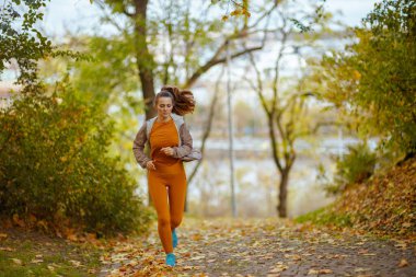 Merhaba sonbahar. Parkta koşu yaparken spor kıyafetleri giymiş zarif bir kadının tam boy portresi..