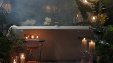 Lüks bir banyoda yeşil, mumlu ve yumuşak sisli modern beyaz bir küvet bulunur. Spa benzeri bir ortam rahatlama ve dinginlik yaratır..