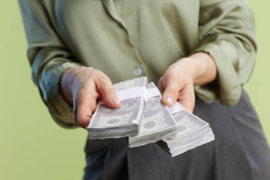 Bir kişi, zenginliği, mali işlemleri ve yumuşak yeşil bir fon karşısında bolluk hissini simgeleyen üç deste Amerikan doları sunuyor..