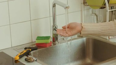 Krom bir musluktan, onarımdan sonra paslanmaz çelik bir lavaboya su akışını test etmek. Yakınlardaki tesisat ve süngerler su kullanımını kontrol ediyor..