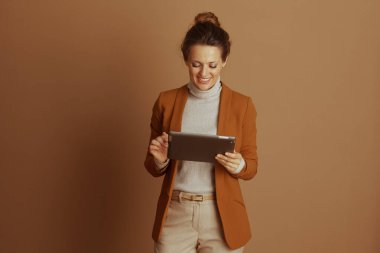 Profesyonel akıllı, sıradan giyinmiş gülümseyen bir kadın koyu gri bir dijital tablet kullanır. Kahverengi saçları topuz gibi, modern çalışma ortamında verimliliği ve bağlılığı yansıtıyor..