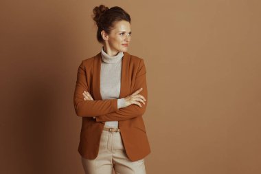 Kahverengi ceket ve bej balıkçı yaka giyen, kollarını kavuşturmuş, kurnazca gülümseyen orta yaşlı, profesyonel bir kadın. Bakışları, kahverengi arka plana karşı düşünceli bir özgüveni olduğunu gösteriyor.