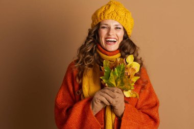 Uzun, kıvırcık kahverengi saçlı, turuncu kazak ve sarı eşarp giyen gülümseyen kadın, elinde bir demet sonbahar yaprağı tutuyor. Bu ortam onun mutluluğunu ve sonbahar mevsiminin sıcaklığını yakalıyor..