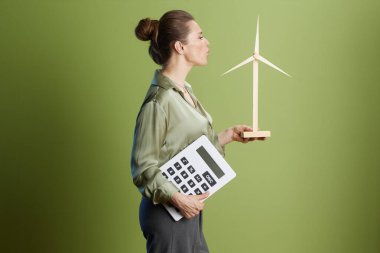 Rüzgar türbini ve hesap makinesi olan kadın yeşil enerji finansmanı öneriyor. Açık yeşil zemine karşı, sürdürülebilir yatırımı sembolize ediyor.