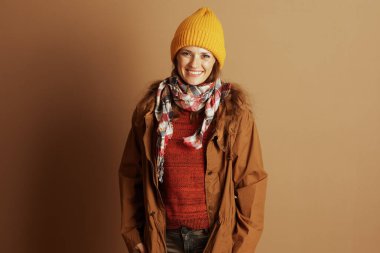 Sarı bereli gülümseyen bir kadın, kırmızı örgü süveter ve ekose eşarp kahverengi bir arka planda duruyor, neşeli, gündelik bir sonbahar modunda ve davetkar bir modda..