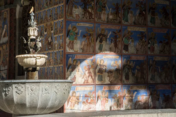 A beautiful small fountain against the background of frescoes of an Orthodox church