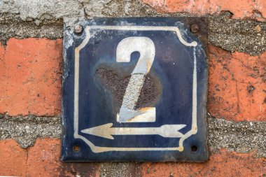 İki numaralı sokak adresinin plakası işlemeli eski püskü, kare bir metal.