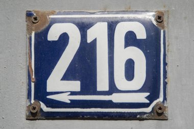 Yıpranmış 216 numaralı sokak adresinin plakası işlemeli eski bir metal parçası.