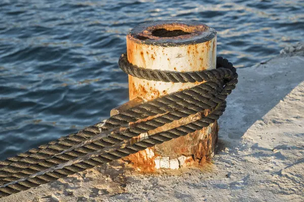 Old metal dock mooring pole with rope for securing fishing boats closeup