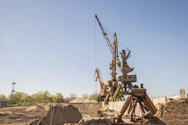 Açık güneşli bir günde sanayi turnaları nehir kumu deposunu boşaltıyor.