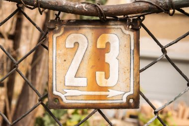 Weathered enameled plate of street address with number 23 clipart