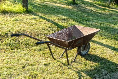 Güneşli kırsal alanda eski, paslı bir el arabası, iyi kullanılmış ve yıpranmış.