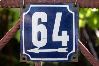 Altında 64 numaralı sokak adresi olan eski püskü, kare bir metal plaka.