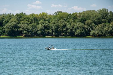 Geniş bir nehri hızla geçen küçük bir motorlu tekne yoluna köpüklü beyaz bir iz bırakıyor.