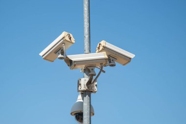 Şehir parkında çoklu modern güvenlik ve güvenlik kameralarıyla donatılmış bir sokak lambası.