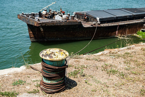 An old, severely rusted river barge moored to a mooring bollard, showcasing low river levels during summer drought