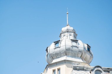 Temiz mavi gökyüzüne karşı kurulmuş, küçük pencereli tarihi bir Avrupa binasının süslü metal kulesi.