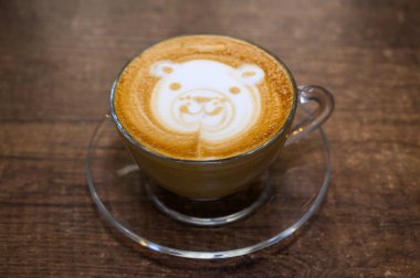 Ahşap bir yüzeyde, berrak bir bardakta servis edilen, ayı yüzlü latte sanatıyla nefis bir bardak kapuçino.