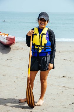 Hayat ceketli gülümseyen kadın güneşli bir plaj gününde su sporlarına hazır.