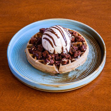 Cömert bir kepçe vanilyalı dondurmayla kaplanmış ve seramik tabağa çikolata sosu serpiştirilmiş görkemli çikolatalı waffle.