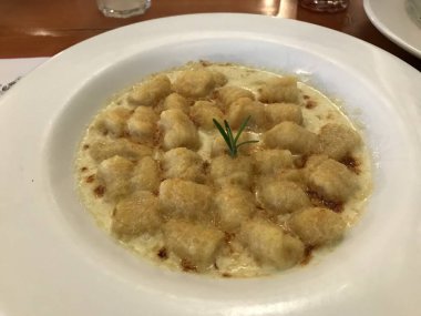 Lezzetli pişmiş gnocchi kremalı sos otlarla süslenmiş, beyaz bir tabakta servis ediliyor.