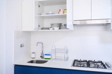 Beyaz dolaplar, mavi aksanlar ve paslanmaz aletlerle dolu parlak, temiz bir mutfak.