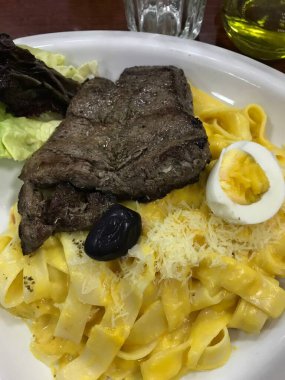 Peynirli makarna ve bir dilim haşlanmış yumurta ile servis edilen iştah açıcı biftek.