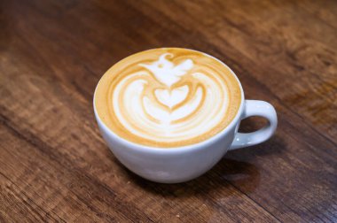 Beyaz bir fincanda servis edilen karışık kalp latte sanatıyla kremalı latte manzarası.