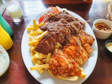 Köy masasında servis edilen et şişleri, patates kızartmaları ve salatadan oluşan karışık ızgara ziyafeti.